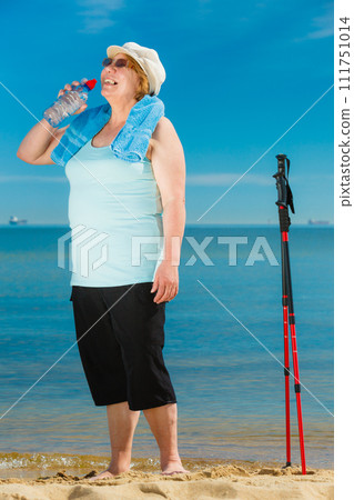 Senior woman practicing nordic walking on beach 111751014
