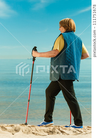 Senior woman practicing nordic walking on beach 111751678