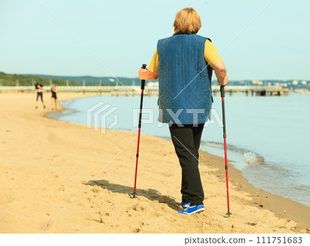 active woman senior nordic walking on a beach. from behind 111751683