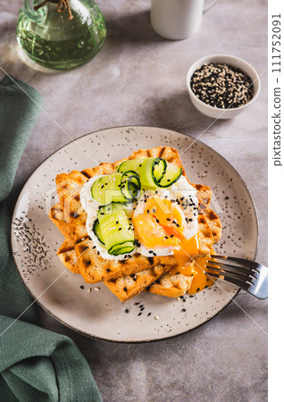 Waffles with poached egg, cucumber and sour cream on a plate on the table vertical view 111752091