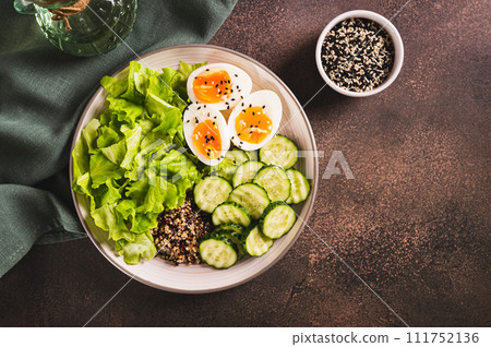 Bowl with quinoa, cucumber, boiled egg, lettuce and sesame seeds on the table top view 111752136