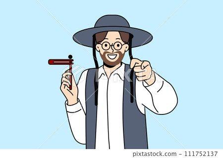 Orthodox jewish man with grager ratchet in hand points finger at screen, during Hanukkah holiday 111752137