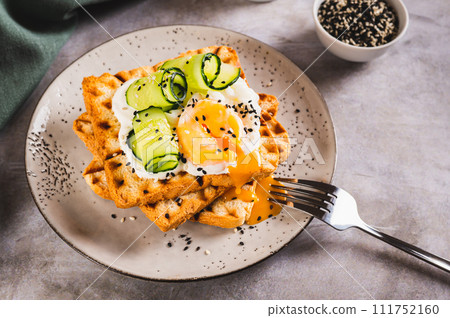 Waffles with poached egg, cucumber and sour cream on a plate on the table Waffles with poached egg, cucumber and sour cream on a plate on the table 111752160