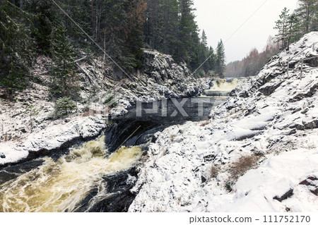 Snowy cascade waterfall. Landscape photo of Kivach Falls on a cold cloudy winter day 111752170