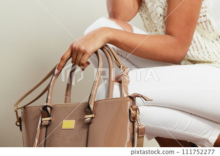 Woman holding beige lacquered leather bag. Woman holding beige lacquered leather bag. 111752277