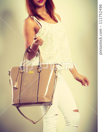Mulatto woman holding beige leather bag. 111752496