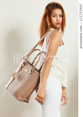 Mulatto woman holding beige leather bag. 111752497