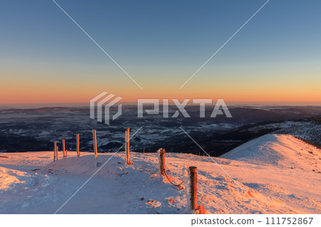 Winter, sunrise time, view from Snezka to pink mountain, krkonose mountain, Czech republic.. Along the road are wooden long bars, tourist markings for winter season. 111752867