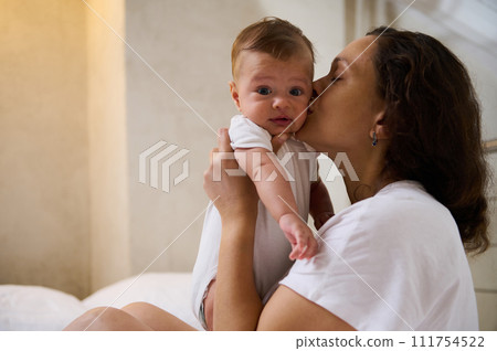 Cute baby boy looking at camera while his mother cuddling and kissing him 111754522