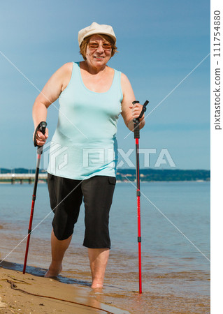 Senior woman practicing nordic walking on beach 111754880