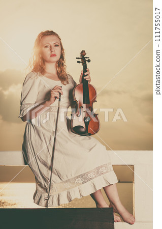 Woman on pier outside holding violin Woman on pier outside holding violin 111755017