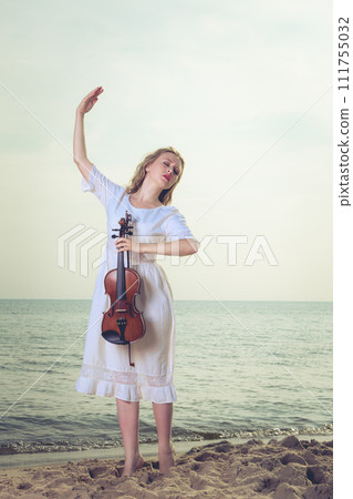 Woman on beach near sea holding violin Woman on beach near sea holding violin 111755032
