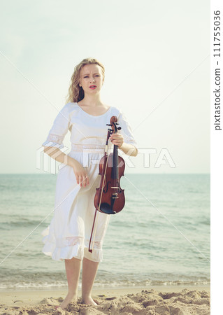 Woman on beach near sea holding violin Woman on beach near sea holding violin 111755036