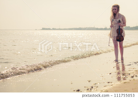 Woman on beach near sea holding violin Woman on beach near sea holding violin 111755053