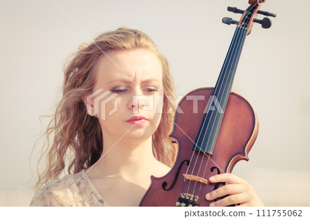 Woman on beach near sea holding violin Woman on beach near sea holding violin 111755062