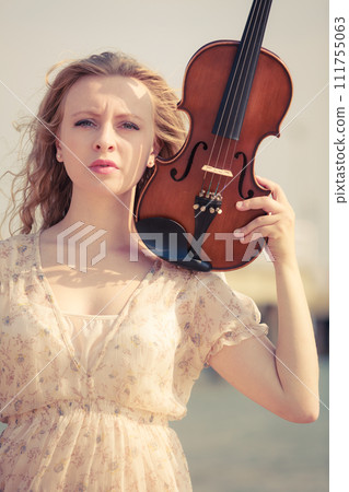 Woman on beach near sea holding violin Woman on beach near sea holding violin 111755063