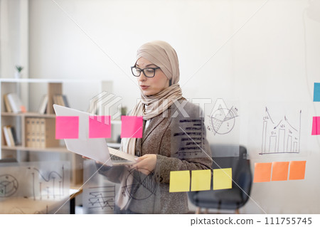 Muslim woman in hijab solving business issues with laptop in hands 111755745