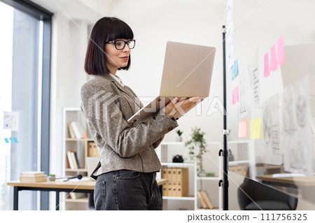 Caucasian woman in formal wear and glasses solving business issues with laptop. 111756325