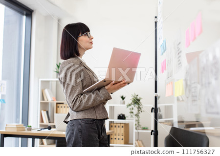 Caucasian woman in formal wear and glasses solving business issues with laptop. Caucasian woman in formal wear and glasses solving business issues with laptop. 111756327
