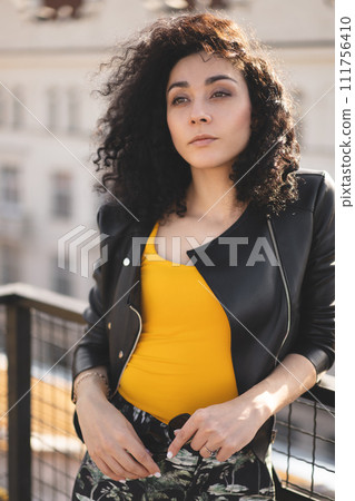 a beautiful girl in a leather jacket poses against the background of the city. a beautiful girl in a leather jacket poses against the background of the city. 111756410