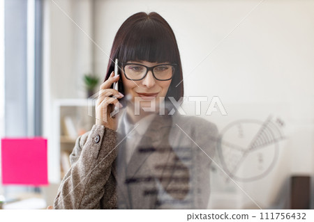 Woman holding talking on smartphone and looking on graphic on glass wall. 111756432