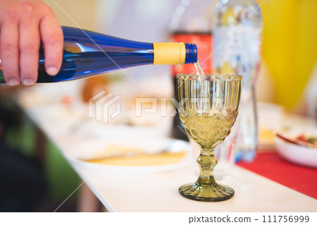 a waiter in a restaurant pours alcohol into a glass at the table 111756999