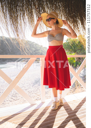 beautiful girl in a red skirt and and a hat in the summer on a terrace on the shore of the sea 111757312