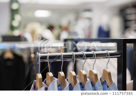 Apparel for sale hanging on metal rack in trendy clothing store. Blue formal male shirts from menswear collection latest arrival on hangers, showcasing for customers in shopping mall 111757385