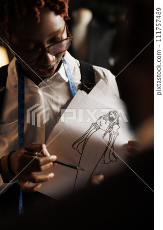 African american dressmaker designing bespoke sartorial collection for upcoming runway fashion show. Creative tailor showing atelier shop workspace coworker stylish dress sketch drawing design African american dressmaker designing bespoke sartorial collection for upcoming runway fashion show. Creative tailor showing atelier shop workspace coworker stylish dress sketch drawing design 111757489