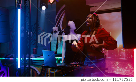 Happy girl putting cool music at club, using DJ mixing station at dance party. Young woman enjoying disco and electronic sounds with friends, dancing and jumping around. Handheld shot. 111757555