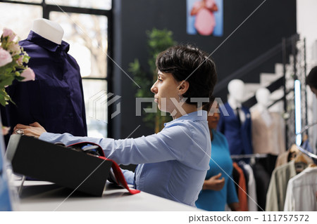 Woman working at boutique opening, arranging stylish clothes and accessories on shelves. Shopping centre manager preparing fashionable merchandise, working with trendy items in clothing store Woman working at boutique opening, arranging stylish clothes and accessories on shelves. Shopping centre manager preparing fashionable merchandise, working with trendy items in clothing store 111757572