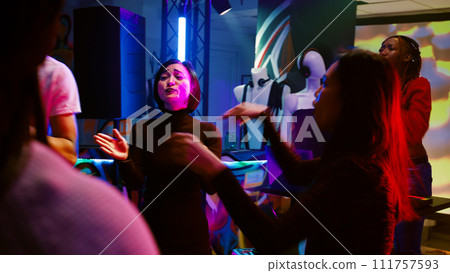 Young persons dancing at club, having fun at disco party on dance floor with funky music. Cheerful group of friends enjoying social gathering at discotheque, colorful lights. Handheld shot. Young persons dancing at club, having fun at disco party on dance floor with funky music. Cheerful group of friends enjoying social gathering at discotheque, colorful lights. Handheld shot. 111757593