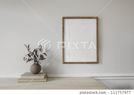Blank vertical wooden picture frame mock up on wooden table. Modern vase with dry eucalyptus tree branches. Pile of vintage books. White wall background. Scandinavian home interior, decor. Blank vertical wooden picture frame mock up on wooden table. Modern vase with dry eucalyptus tree branches. Pile of vintage books. White wall background. Scandinavian home interior, decor. 111757977
