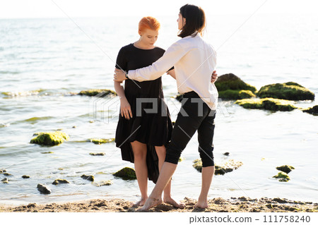 two lovers boy and girl are happy walking and hugging on the sandy beach near the sea. two lovers boy and girl are happy walking and hugging on the sandy beach near the sea. 111758240