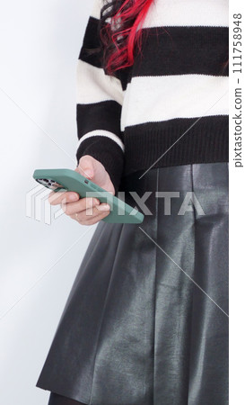 Teenager girl in a white and black sweater and leather skirt is using smart phone. Faceless, vertical. Social media, music, testing, online shopping. Teenager girl in a white and black sweater and leather skirt is using smart phone. Faceless, vertical. Social media, music, testing, online shopping. 111758948