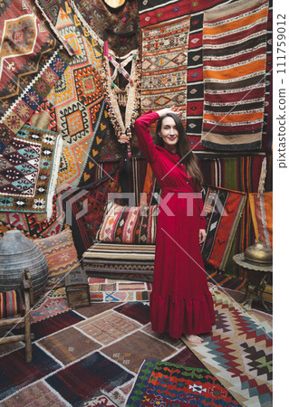 a beautiful girl in a red dress in a traditional turkish interior with many carpets on the wall 111759012