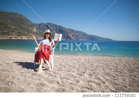 happy girl in a red skirt on an empty beach sits on a chair and reads a book happy girl in a red skirt on an empty beach sits on a chair and reads a book 111759102
