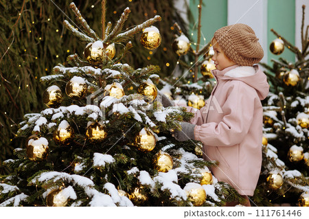 Child in a coat near a snow-covered Christmas tree 111761446