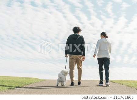 Rear view of a family, couple, man and woman walking their dog in the park Rear view of a family, couple, man and woman walking their dog in the park 111761665