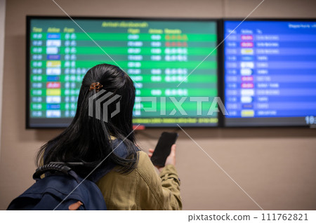 A back view shot of a female passenger checking her boarding time on a monitor screen in the airport. 111762821