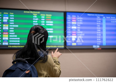 A back view shot of a female passenger checking her boarding time on a monitor screen in the airport. 111762822
