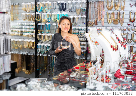 Young positive woman choosing necklace in shop Young positive woman choosing necklace in shop 111763032