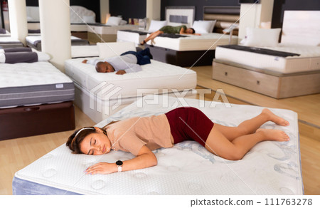 Portrait of tired latin american girl sleeping on modern orthopedic mattress in furniture showroom Portrait of tired latin american girl sleeping on modern orthopedic mattress in furniture showroom 111763278