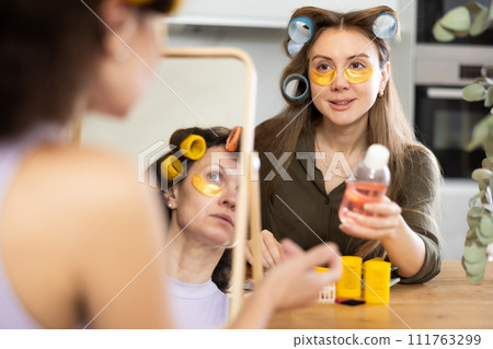Women in colorful curlers applying eye patches and sharing beauty secrets 111763299