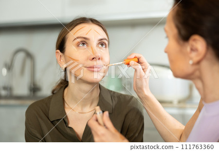 Makeup artist contouring young woman face in home setting Makeup artist contouring young woman face in home setting 111763360