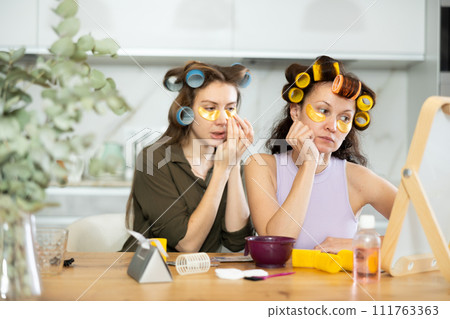 Two women curl their hair with curlers and use patches 111763363