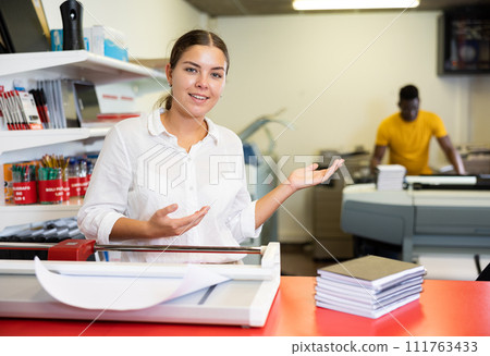 Portrait of happy young female typographer using paper cutter cutter during work in the printer shop 111763433