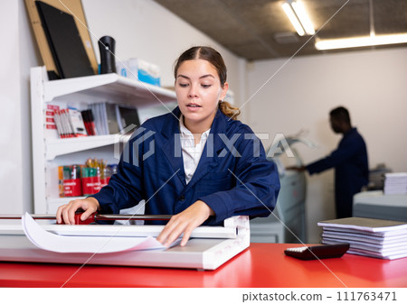 Work in printing house - woman cuts paper with professional cutter 111763471