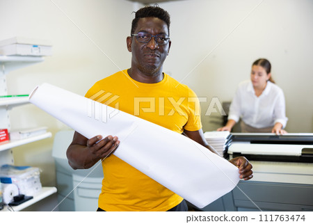 Middle-aged African American man holding large format paper whatman in a roll in the middle of the typography Middle-aged African American man holding large format paper whatman in a roll in the middle of the typography 111763474