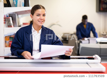 Excited young female in a blue uniform holding empty sheet during work in the typography 111763509